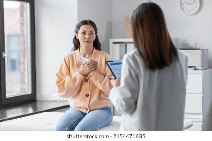 medicine, healthcare and people concept - female doctor with clipboard talking to woman holding to her chest patient at hospital