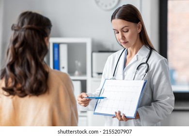 Medicine, Healthcare And People Concept - Female Doctor Or Cardiologist With Clipboard Showing Cardiogram To Woman Patient At Hospital