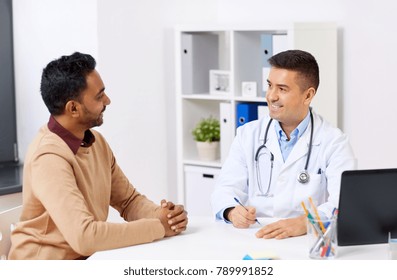 Medicine, Healthcare And People Concept - Happy Doctor Writing Prescription For Male Patient At Clinic