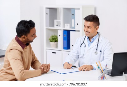 Medicine, Healthcare And People Concept - Happy Doctor With Clipboard And Young Male Patient Meeting At Hospital