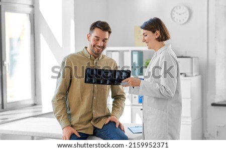 medicine, healthcare and people concept - happy smiling female doctor showing x-ray to male patient at medical office in hospital