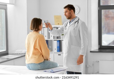 medicine, healthcare and people concept - male doctor with infrared forehead thermometer measuring temperature of woman patient at hospital