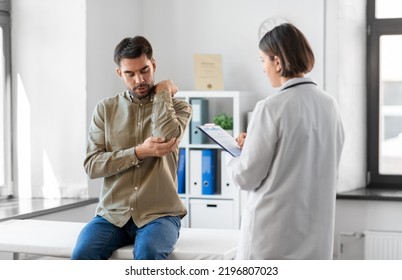 Medicine, Healthcare And People Concept - Male Patient Showing Sore Arm To Female Doctor At Medical Office In Hospital