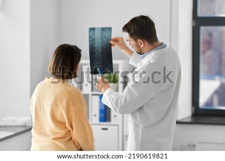 medicine, healthcare and people concept - male doctor showing x-ray to female patient at medical office in hospital