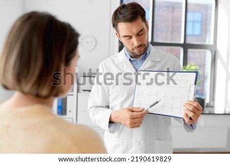 medicine, healthcare and people concept - male doctor or cardiologist with clipboard showing cardiogram to woman patient at hospital