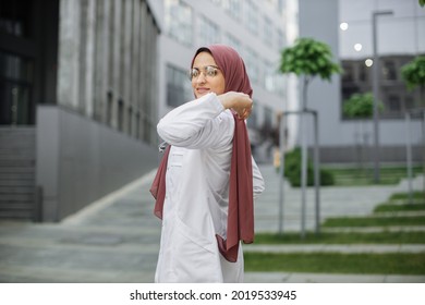 Medicine And Healthcare. Portrait Of Pretty Saudi Arabian Muslim Doctor Or Nurse Woman In White Coat With Stethoscope, Adjusting Her Hijab And Looking At Camera. Outdoor Portrait Of Arab Lady Doctor