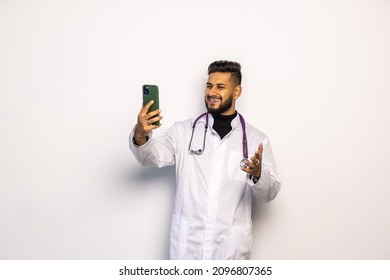 Medicine, Healthcare And Technology Concept - Happy Smiling Indian Doctor Or Male Nurse In Uniform Having Video Call On Phone Over White Background