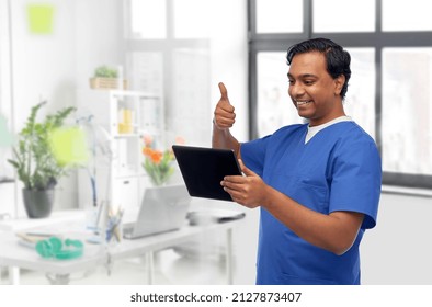 medicine, healthcare and technology concept - happy smiling doctor or male nurse having video call on tablet pc computer and showing thumbs up over medical office at hospital background