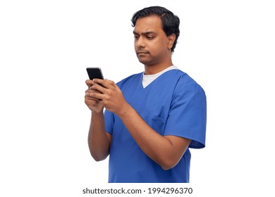 Medicine, Healthcare And Technology Concept - Indian Doctor Or Male Nurse In Blue Uniform Using Smartphone Over White Background