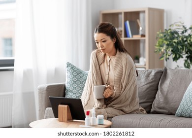 Medicine, Healthcare And Technology Concept - Sick Young Asian Woman Having Video Call Or Online Consultation On Tablet Pc Computer And Drinking Tea At Home