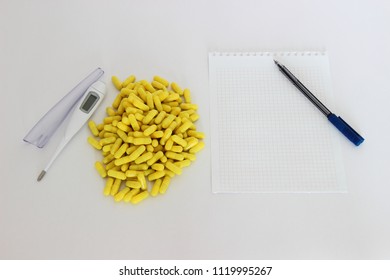 Medicine, medication, healing – many yellow capsules next to the white digital thermometer and paper for the inscription with a pen (copy space) - Shutterstock ID 1119995267