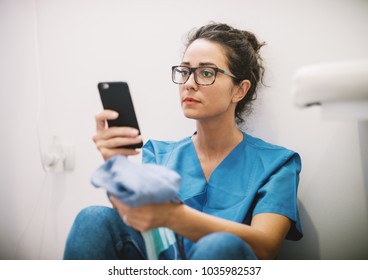 Medicine nurse sitting on the floor looking sadly at smart phone. - Powered by Shutterstock