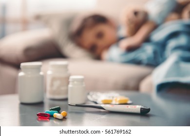 Medicine on the table, in the background sick little girl is lying on couch