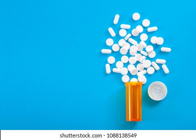 Medicine, opioid painkillers and prescription medicines concept with top view of orange prescription bottle of oxycodone and hydrocodone pills spilled on a blue background with copy space