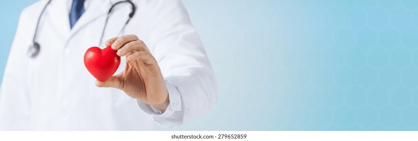 Medicine, People, Charity, Health Care And Cardiology Concept - Close Up Of Male Doctor Hand Holding Red Heart Over Blue Background