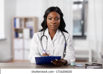 medicine, people and healthcare concept - african american female doctor or nurse writing medical report to clipboard at hospital