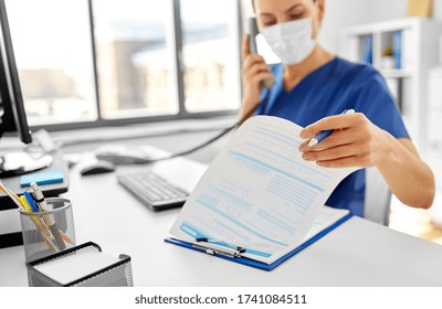 medicine, people and healthcare concept - female doctor or nurse wearing face protective medical mask for protection from virus disease with computer and clipboard calling on phone at hospital - Powered by Shutterstock