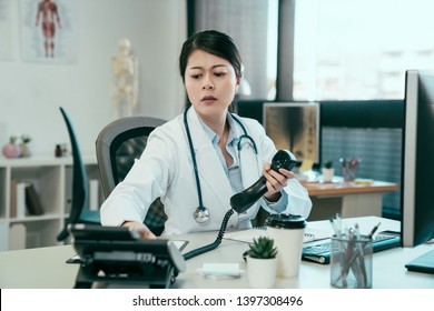 Medicine People And Healthcare Concept. Frowning Asian Female Doctor With Computer Calling On Phone At Hospital. Confused Young Girl Intern Nurse Having Problem Using Telephone To Contact Colleague.