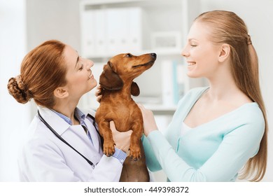 Medicine, Pet Care And People Concept - Happy Woman And Veterinarian Doctor Holding Dachshund Dog At Vet Clinic