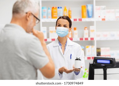 Medicine, Pharmaceutics, Health Care And People Concept - Apothecary Wearing Face Protective Medical Mask For Protection From Virus Disease Showing Drug To Senior Man Customer At Drugstore