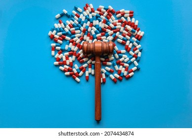Medicine pills or capsules with a gavel on blue background. Drugs and law concept.