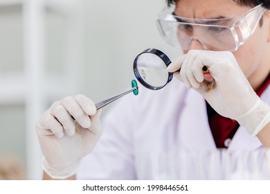 Medicine Production Quality Assurance And Care Concept. Scientist In Medical Factory Using Magnifying Glass To Checking Defective Medical Pill Products.