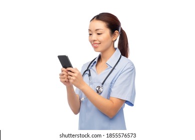 Medicine, Profession And Healthcare Concept - Happy Smiling Asian Female Doctor Or Nurse In Blue Uniform With Stethoscope Using Smartphone Over White Background