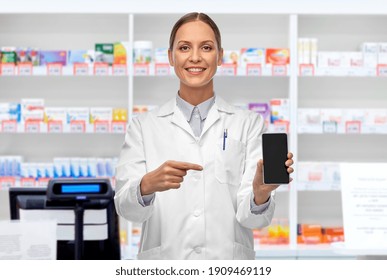 medicine, profession and healthcare concept - happy smiling female doctor or scientist showing smartphone over pharmacy background