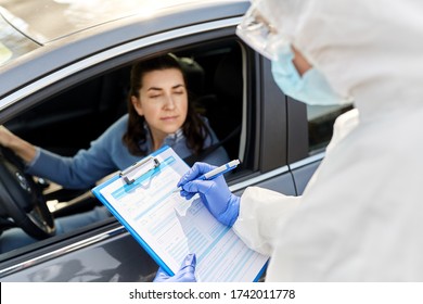 Medicine, Quarantine And Pandemic Concept - Doctor Or Healthcare Worker In Protective Gear Or Hazmat Suit, Medical Mask And Gloves With Clipboard And Woman Waiting For Coronavirus Test In Her Car