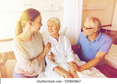 Medicine, Support, Family Health Care And People Concept - Happy Senior Man And Young Woman Visiting And Cheering Her Grandmother Lying In Bed At Hospital Ward