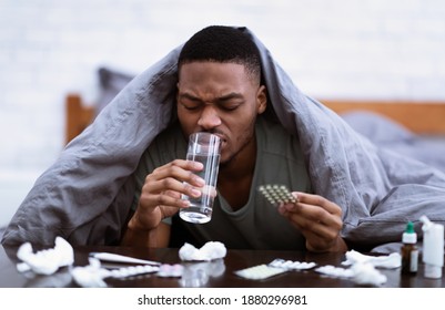 Medicine Treatment. Sick African American Man Taking Pills Drinking Water Lying In Bed At Home, With Many Medication Tablets And Painkilling Capsules. Healthcare, Medical Drugs Prescription