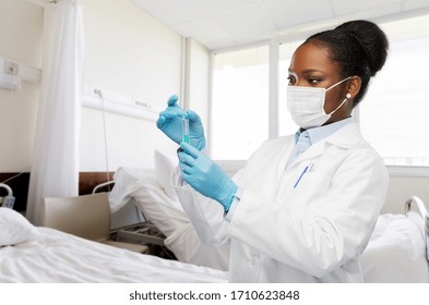 medicine, vaccination and healthcare concept - african american female doctor in mask with syringe over hospital ward background