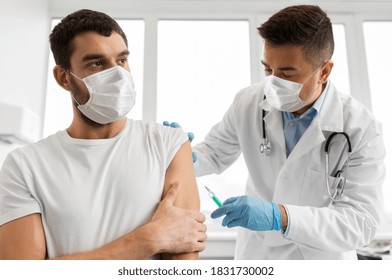 medicine, vaccination and healthcare concept - doctor with syringe doing injection of vaccine to male patient wearing face protective medical masks for protection from virus disease - Shutterstock ID 1831730002