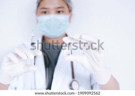 Medicine, vaccination, immunization and healthcare concept. Asian female doctor or scientist wearing mask with syringe and liquid vaccines in hand on white background