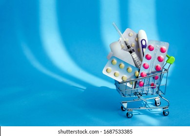 Medicines And Pills In A Shopping Cart  On Blue Background. Consumer Buying Panic About Coronavirus Covid-19 Concept.  First Aid Kit For Home Quarantine. Drug Delivery. Copy Space