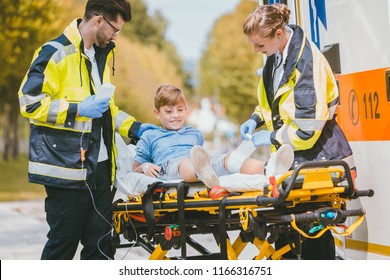 Medics putting injured boy on stretcher after accident in front of ambulance car - Powered by Shutterstock