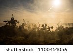 Medieval battle scene with cavalry and infantry. Silhouettes of figures as separate objects, fight between warriors on sunset foggy background. Selective focus