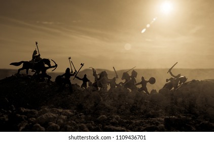 Medieval battle scene with cavalry and infantry. Silhouettes of figures as separate objects, fight between warriors on sunset foggy background. Selective focus - Shutterstock ID 1109436701