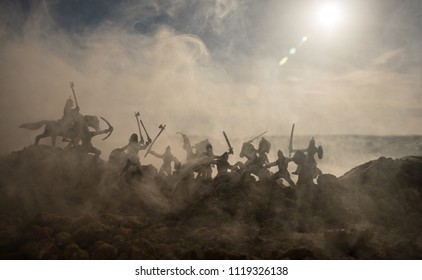Medieval battle scene with cavalry and infantry. Silhouettes of figures as separate objects, fight between warriors on sunset foggy background. Selective focus - Shutterstock ID 1119326138