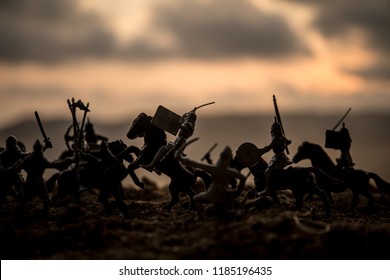 Medieval battle scene with cavalry and infantry. Silhouettes of figures as separate objects, fight between warriors on sunset foggy background. Selective focus - Shutterstock ID 1185196435