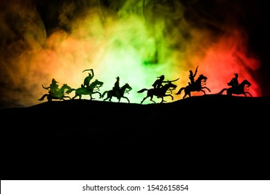 Medieval battle scene with cavalry and infantry. Silhouettes of figures as separate objects, fight between warriors on dark toned foggy background. Night scene. Selective focus