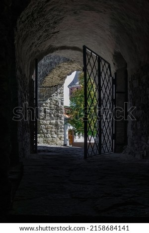 Medieval castle arc passageway. Arc passageway from cold damp blackness to glow light with rusted iron grate cell. 