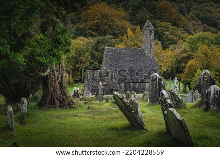 Medieval church, ancient graves, Celtic crosses in Glendalough Cemetery with autumn forest and mountains in the background, Wicklow, Ireland