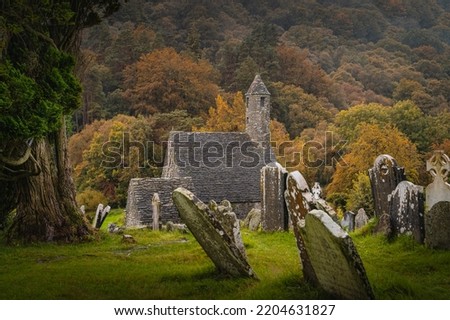 Medieval church, ancient graves, Celtic crosses in Glendalough Cemetery with autumn forest and mountains in the rain at background, Wicklow, Ireland