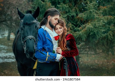 Medieval Couple In Love Man And Woman Hugging In Winter Forest. Vintage Clothing Red Long Dress. Blue Costume Tailcoat Caftan. Prince And Princess Together. Black Horse. Art Image Redhead Hairstyle