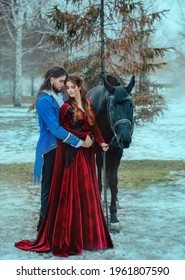 Medieval couple in love man and woman hugging in winter forest. Vintage clothing red long dress. Blue frock coat costume, tailcoat caftan. Prince and princess together. Black steed horse. Art image.