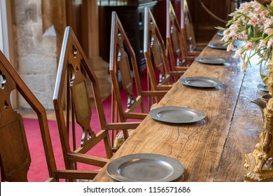 Medieval Dining Table And Chairs. Mediaeval Period Banquet Table Set With Metal Plates. Fine Historic Fraternal Banqueting Hall. Secret Society Chamber With Anonymous Empty Seats.