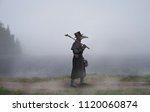 Medieval era. The plague doctor walks along the road near the misty lake