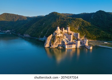 The medieval fortress of Golubac, mirroring in the waters of the Danube. Fortress towers illuminated by warm sunset light, blue sky. Aerial shot. Famous tourist place, Serbia. - Shutterstock ID 2074197314