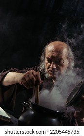 Medieval Healer Preparing Magic Potion In Boiling Pot Isolated On Black